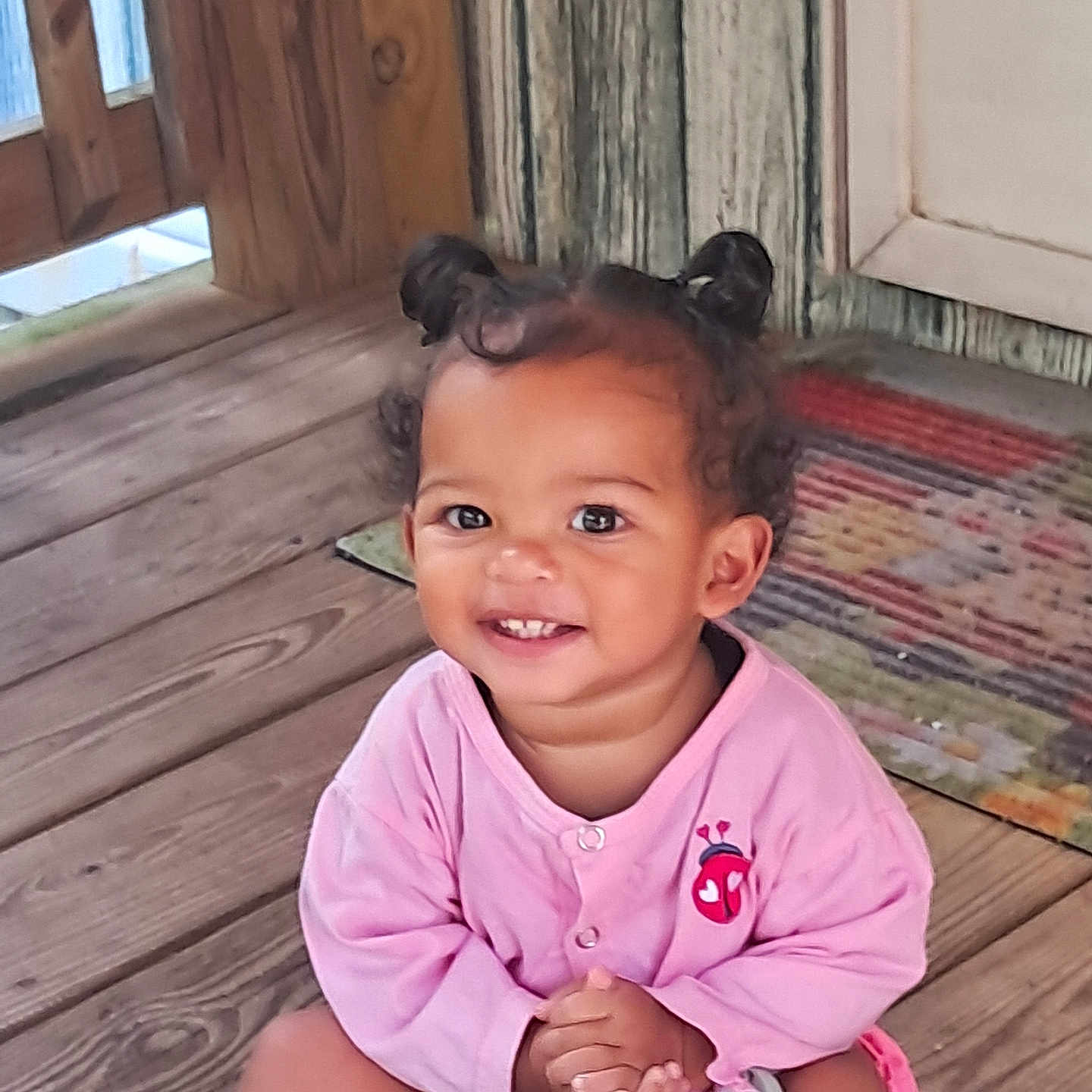 Chianne is registered to the contest to win money with this photo: baby, casual_clothing, child, cute, cute_hair, decor, hair_buns, hands_clasped, happy, indoor, person, pink_clothing, playful, portrait, rug, sitting, smiling, toddler, wooden_floor, young_child