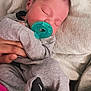 baby, newborn, infant, pacifier, sleeping, sleeping_baby, blanket, pillow, onesie, gray_clothing, hand, parent_hand, close_up, portrait, indoors, cute, cozy, small_size, skin, head