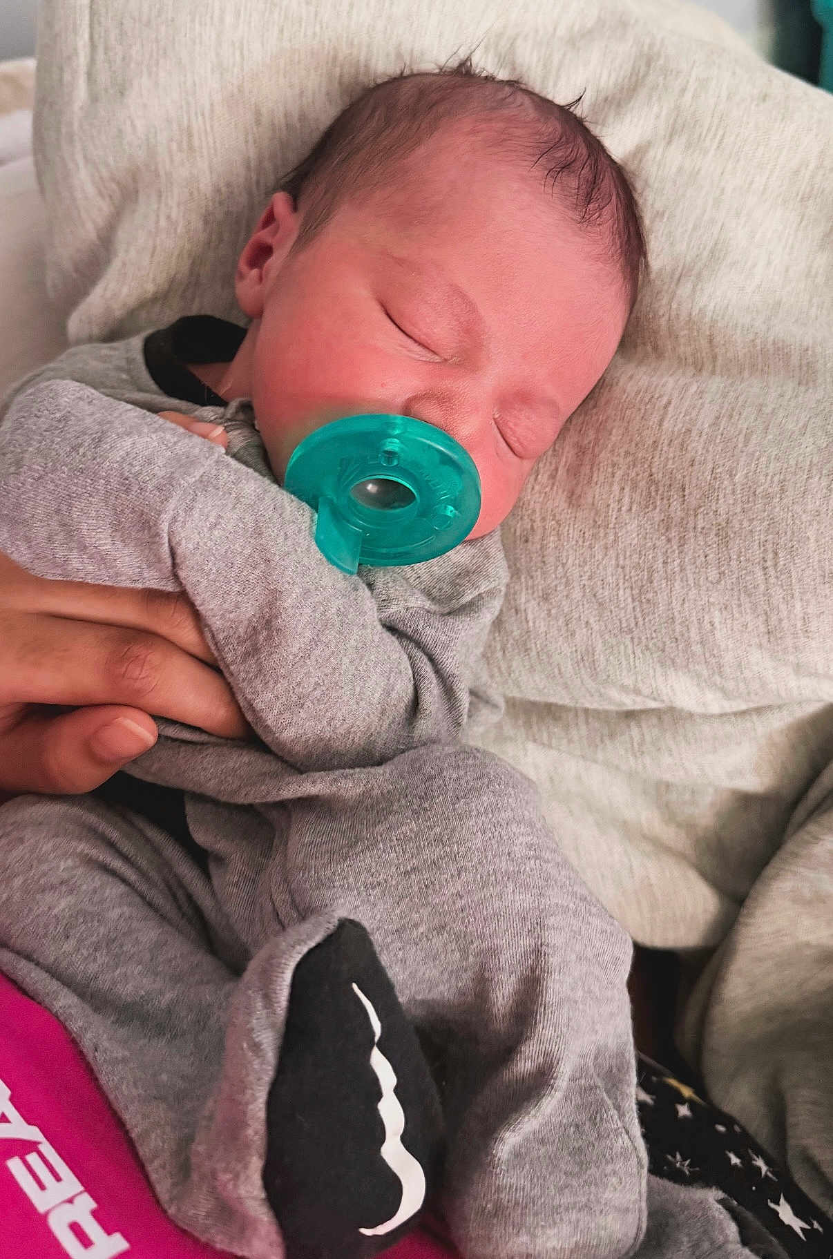 Grayson is registered to the contest to win money with this photo: baby, newborn, infant, pacifier, sleeping, sleeping_baby, blanket, pillow, onesie, gray_clothing, hand, parent_hand, close_up, portrait, indoors, cute, cozy, small_size, skin, head