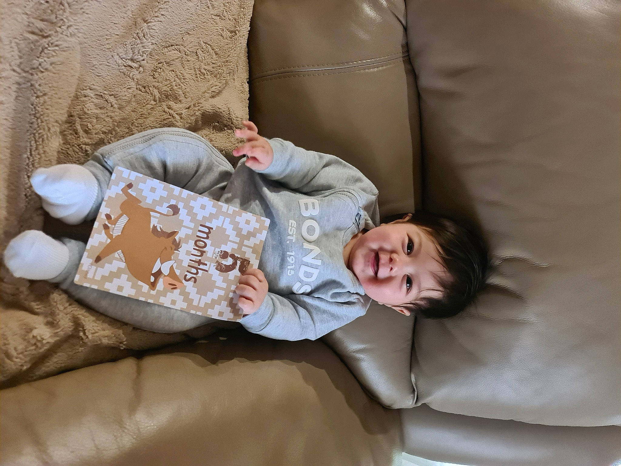 Zaire is registered to the contest to win money with this photo: baby, bedding, child, comfort, couch, happy, joy, leg, linens, mammal, person, product, room, sitting, sleeve, smile, suit, textile, throw_pillow, toddler