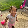 toddler, child, braided_hair, outdoor, sunlight, grass, playful, sporty_clothing, pink_pants, gray_shirt, sneakers, face, person, standing, toy, chair, happy, daylight, portrait, expression