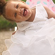 Tori Jones joined the competition — help win amazing prizes! child, toddler, smiling, white_dress, curly_hair, earrings, chair, outdoor, green_background, happy, portrait, cute, joyful, person, fashion, sitting, daylight, young, pretty, fun