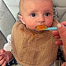 apparel, baby, bib, child, clothing, cute, expression, face, feeding, food, hand, high_chair, indoor, infant, person, puree, seatbelt, skin, spoon, young