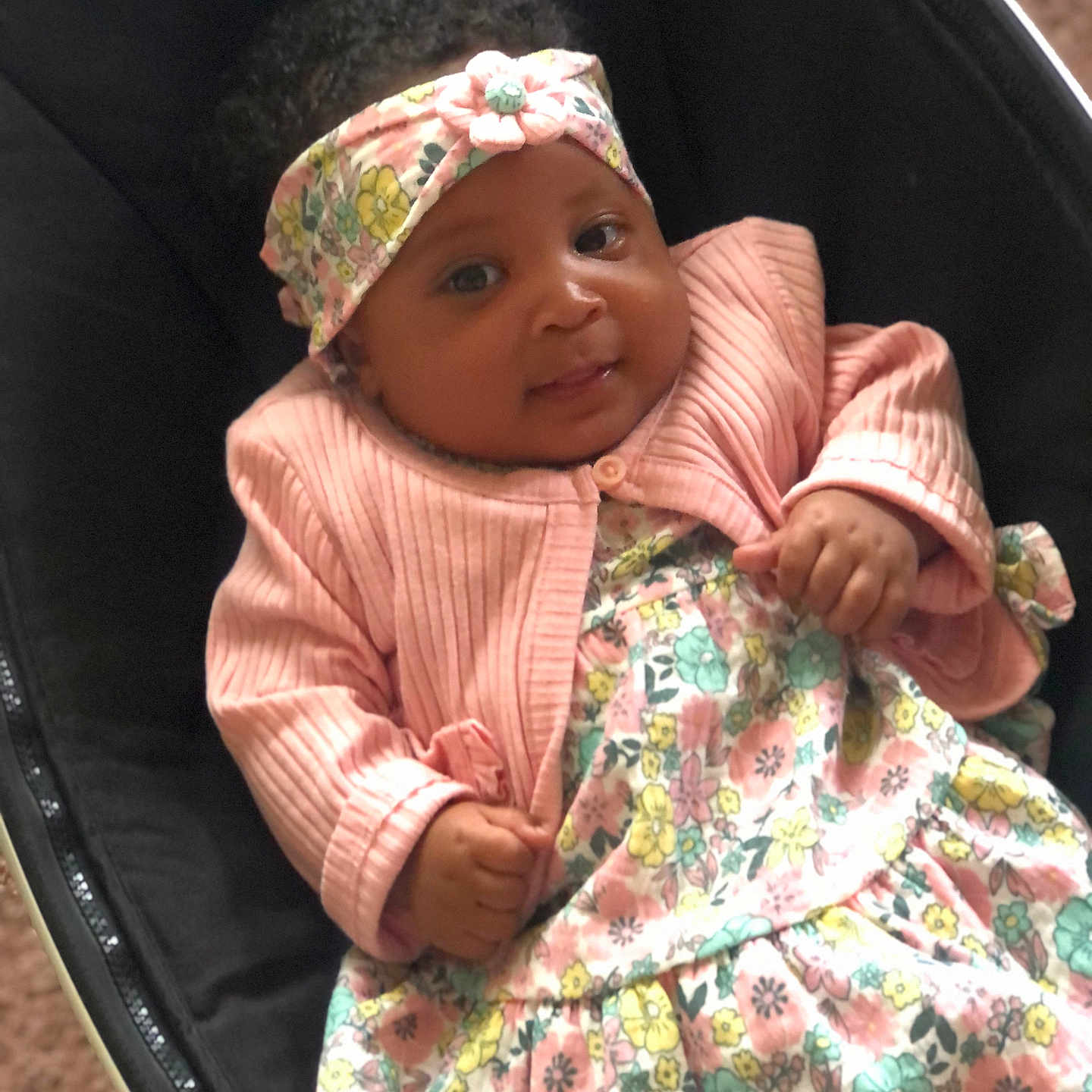 Rahnearah is registered to the contest to win money with this photo: adorable, baby, black_seat, child, clothing, comfortable, cozy, cute, expression, face, floral_dress, hands, headband, indoors, infant, pink_jacket, portrait, seat, smiling, young_child