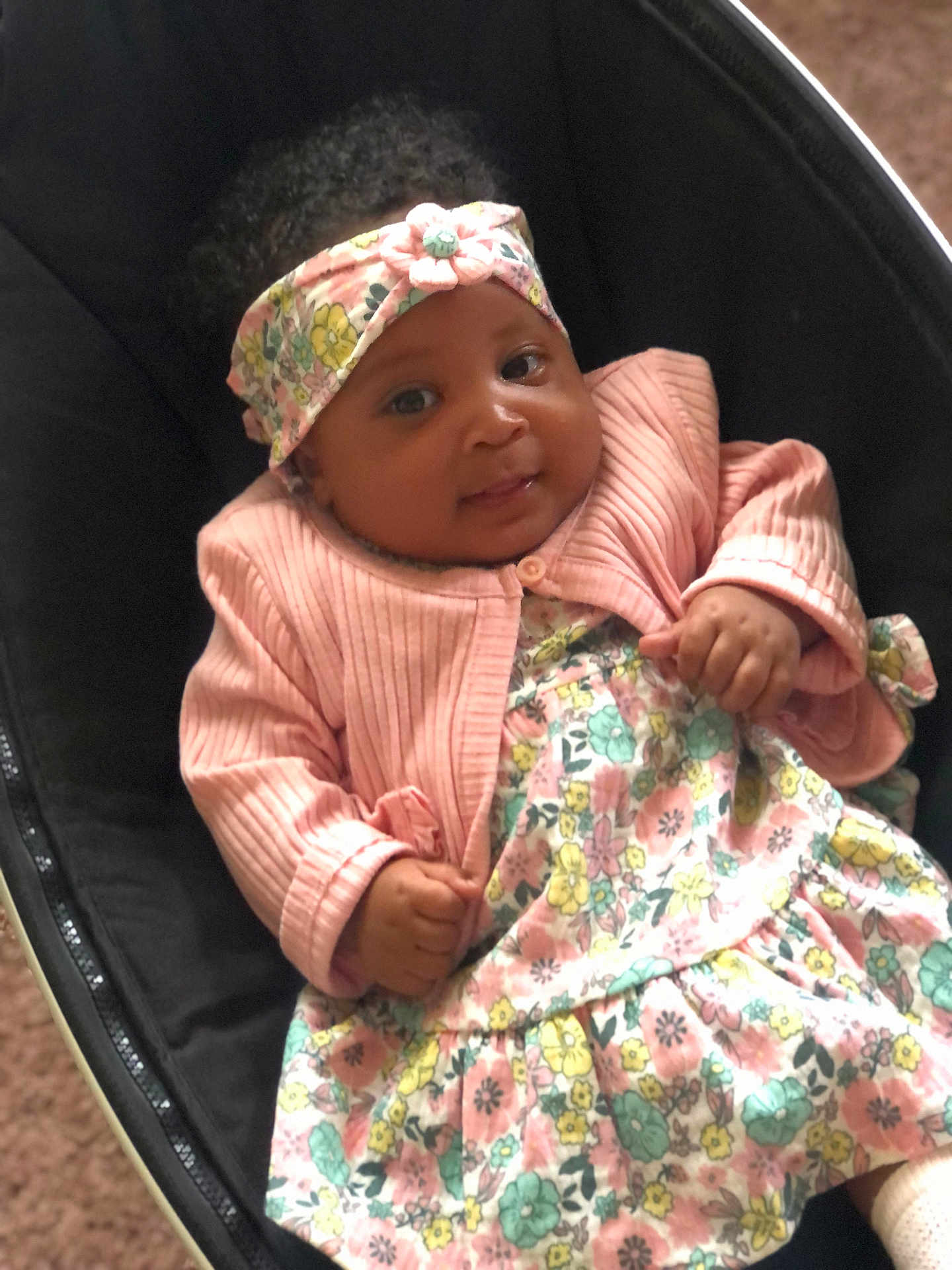 Rahnearah is registered to the contest to win money with this photo: baby, infant, child, headband, pink_jacket, floral_dress, smiling, cute, portrait, indoors, seat, black_seat, hands, face, expression, young_child, cozy, comfortable, clothing, adorable