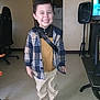 Bellamy joined the competition — help win amazing prizes! child, smiling, indoor, plaid_jacket, yellow_shirt, beige_pants, brown_shoes, standing, happy, person, floor, chair, speaker, television, room, home, furniture, casual_clothing, portrait, young_boy