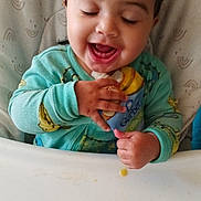 Krisus joined the competition — help win amazing prizes! baby_food, child, closed_eyes, cute, face, feeding, food_pouch, green_clothing, hand, happy, high_chair, indoor, infant, messy, person, seat, smiling, snack, table, toddler