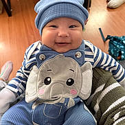 Jameson joined the competition — help win amazing prizes! baby, smiling, blue_hat, elephant_overalls, striped_sleeves, indoor, wooden_floor, cute, child, happy, person, clothing, infant, holding, apparel, face, headwear, sitting, young_child, cozy