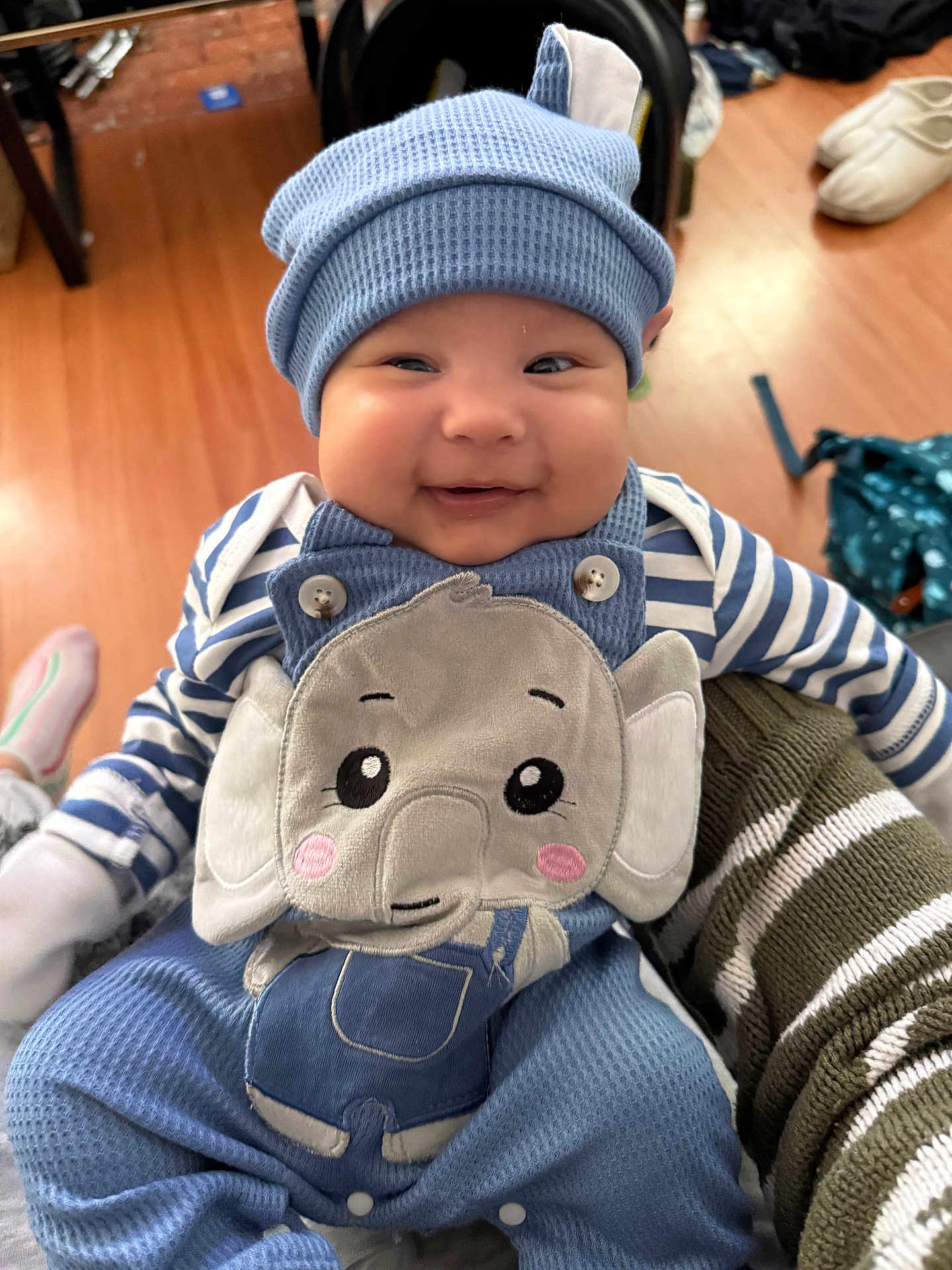 Jameson joined the competition — help win amazing prizes! baby, smiling, blue_hat, elephant_overalls, striped_sleeves, indoor, wooden_floor, cute, child, happy, person, clothing, infant, holding, apparel, face, headwear, sitting, young_child, cozy