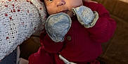 Jameson is registered to the contest to win money with this photo: baby, child, closeup, couch, cozy, cute, hand, hat, indoor, infant, knitwear, mittens, moccasins, person, portrait, red_clothing, seated, soft_lighting, warm_colors, wood_floor