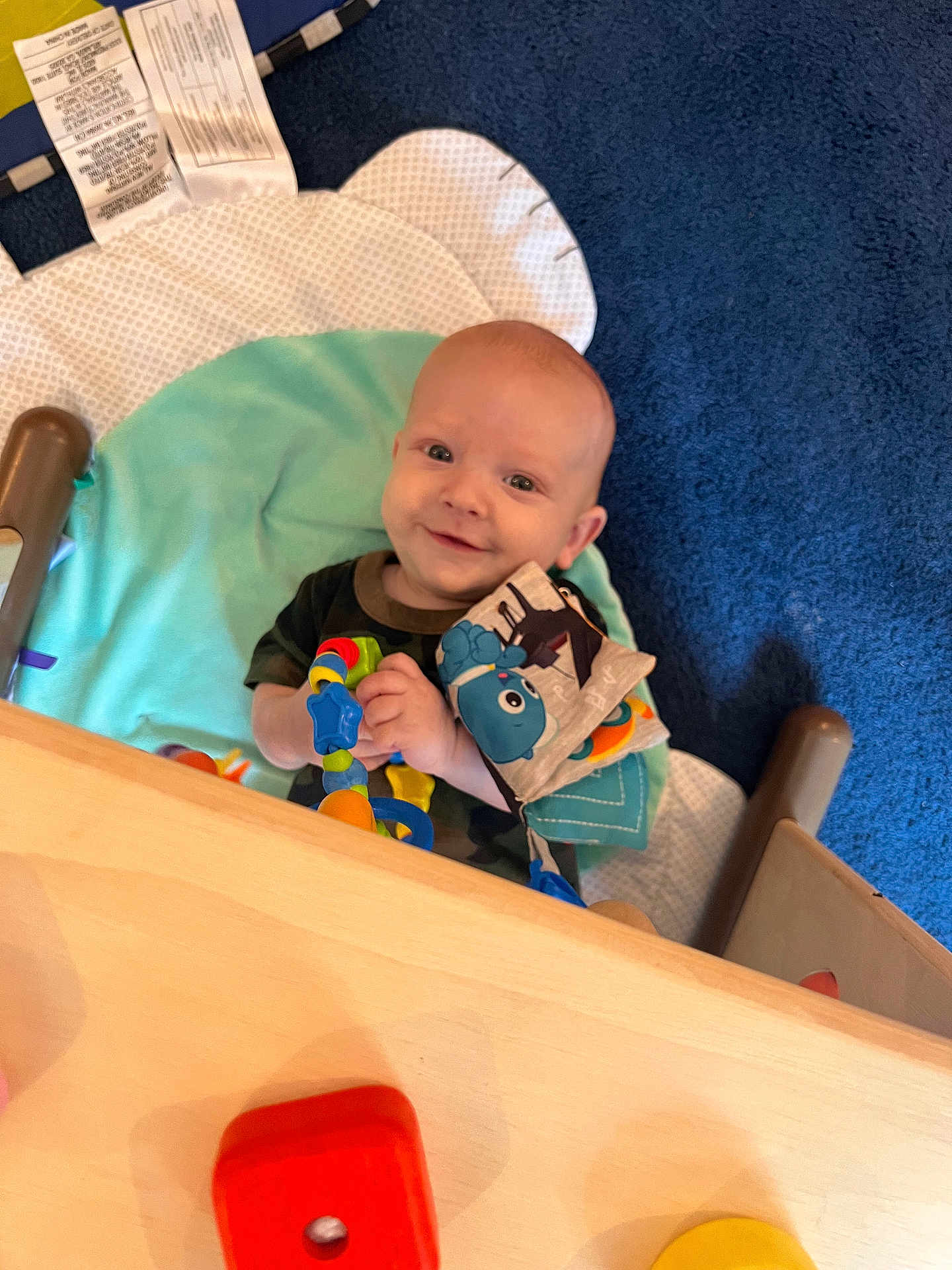 Colton is registered to the contest to win money with this photo: baby, smiling, toy, play_mat, blue_carpet, wooden_toy, infant, child, indoor, colorful, cute, happy, playtime, person, soft_toy, floor, cushion, clothing, head, hands