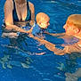 woman, baby, man, swimming_pool, water, glasses, summer, outdoor, sunlight, blue, baby_swimming, family, fun, playful, people, casual, sitting, interaction, relaxation, leisure