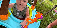 Greyson joined the competition — help win amazing prizes! baby, child, blue_eyes, activity_center, toy_giraffe, toy_lion, grass, summer, outdoor, feet, flip_flops, greenery, playtime, infant, cute, curious, person, clothing, hand, foot