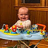 Montgomery is registered to the contest to win money with this photo: baby, child, infant, smiling, sitting, walker, activity_center, toys, colorful, indoor, portrait, wood_paneling, window, home, clothing, long_sleeves, striped_pants, socks, happy, playtime