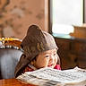 Nathan is registered to the contest to win money with this photo: child, toddler, baby, portrait, smiling, happy, face, hat, traditional_clothing, book, reading, indoors, vintage, wooden_table, chair, window, warm_lighting, library, close_up, photography
