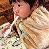 toddler, child, baby, portrait, face, eyes, hair, blanket, bundled_up, straw, spoon, pacifier, activity_book, illustrations, wooden_background, indoor, cozy, sitting, close_up, adorable
