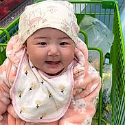 Naomi joined the competition — help win amazing prizes! baby, child, shopping_cart, grocery_store, produce, red_peppers, green_peppers, bib, hat, pink_onesie, smiling, face, cute, indoor, person, clothing, food, shopping, happy, infant
