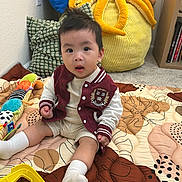 Eugene Vang joined the competition — help win amazing prizes! toddler, child, baby, toy, plush, octopus, quilt, colorful, socks, sitting, indoor, carpet, pillow, cushion, sleeveless, jacket, curious, face, person, room
