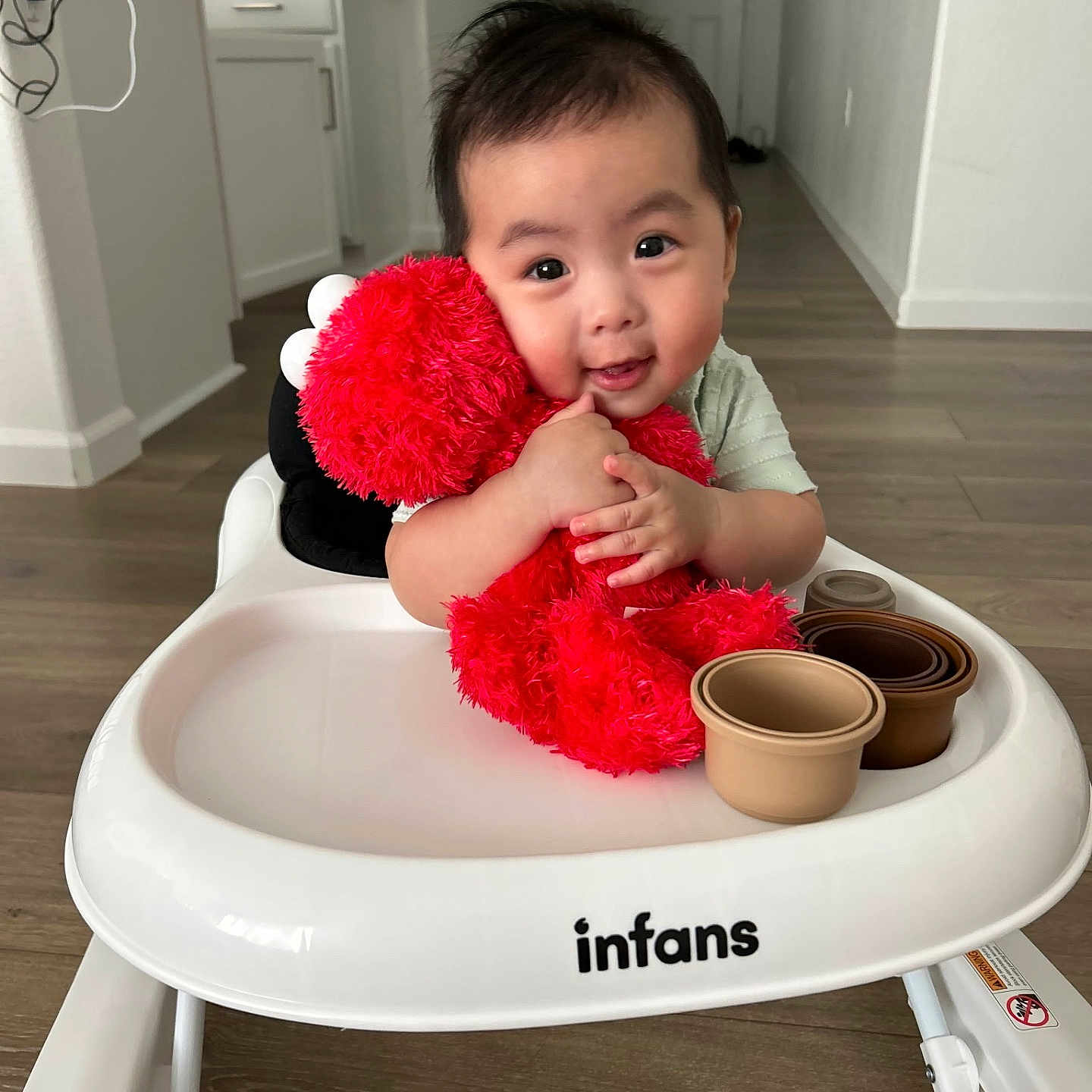 Eugene Vang is registered to the contest to win money with this photo: baby, child, cute, elmo, floor, happy, home, indoor, infans, kitchen, light, person, plush_toy, red, sitting, smiling, stacked_cups, toy, walker, wooden_floor