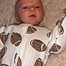 Winston is registered to the contest to win money with this photo: baby, infant, onesie, football_pattern, blanket, soft_texture, sleepwear, child, portrait, cute, lying_down, indoors, comfortable, young_child, face, head, expression, white_clothing, brown_pattern, cozy