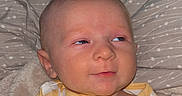 Winston is registered to the contest to win money with this photo: baby, child, infant, onesie, yellow, white, checkered, pillow, blanket, face, head, skin, eyes, expression, lying_down, indoors, portrait, cute, smile, baby_clothes