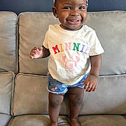 Jehcey is registered to the contest to win money with this photo: toddler, child, smiling, standing, couch, indoor, clothing, headband, shorts, barefoot, happy, person, cute, young_child, portrait, home, furniture, skin, face, apparel