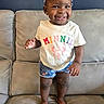toddler, child, smiling, standing, couch, indoor, clothing, headband, shorts, barefoot, happy, person, cute, young_child, portrait, home, furniture, skin, face, apparel