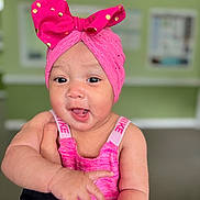 Diana is registered to the contest to win money with this photo: baby, child, pink_headwrap, polka_dots, smiling, reaching_hand, indoors, blurred_background, cute, happy, portrait, closeup, headwear, infant, person, bright_colors, skin, expression, clothing, fashion