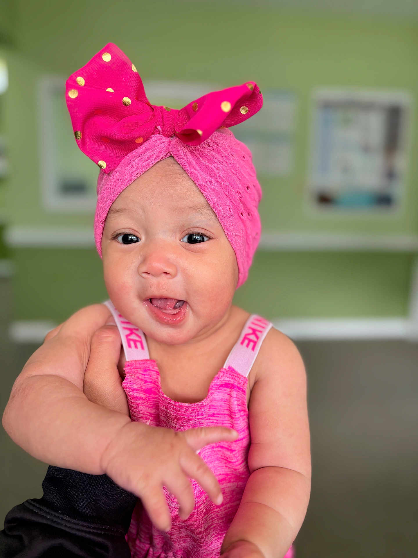 Diana is registered to the contest to win money with this photo: baby, child, pink_headwrap, polka_dots, smiling, reaching_hand, indoors, blurred_background, cute, happy, portrait, closeup, headwear, infant, person, bright_colors, skin, expression, clothing, fashion