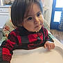 toddler, child, high_chair, red_sweater, black_sweater, checkered_pattern, indoor, kitchen, curious, face, person, long_hair, hand, table, furniture, baby, seat, expression, young_child, portrait