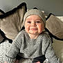 baby, child, smiling, knitted_hat, grey_sweater, blanket, cushion, cozy, indoors, cute, happy, portrait, infant, sitting, soft_lighting, home, warm_clothing, foot, hand, face