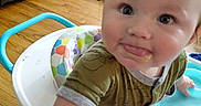 Isaac is registered to the contest to win money with this photo: baby, child, infant, portrait, face, tongue_out, curious, indoors, living_room, walker, baby_walker, toy, rattle, mirror, colorful, wood_floor, furniture, chair, smiling, close_up