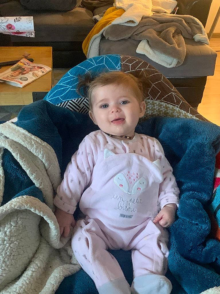 Enola a rejoint le concours — aidez-le/la à gagner de superbes lots ! baby, baby_products, baby_toddler_clothing, box, chair, cheek, child, comfort, couch, event, fashion_accessory, happy, lap, linens, person, product, room, sitting, smile, textile