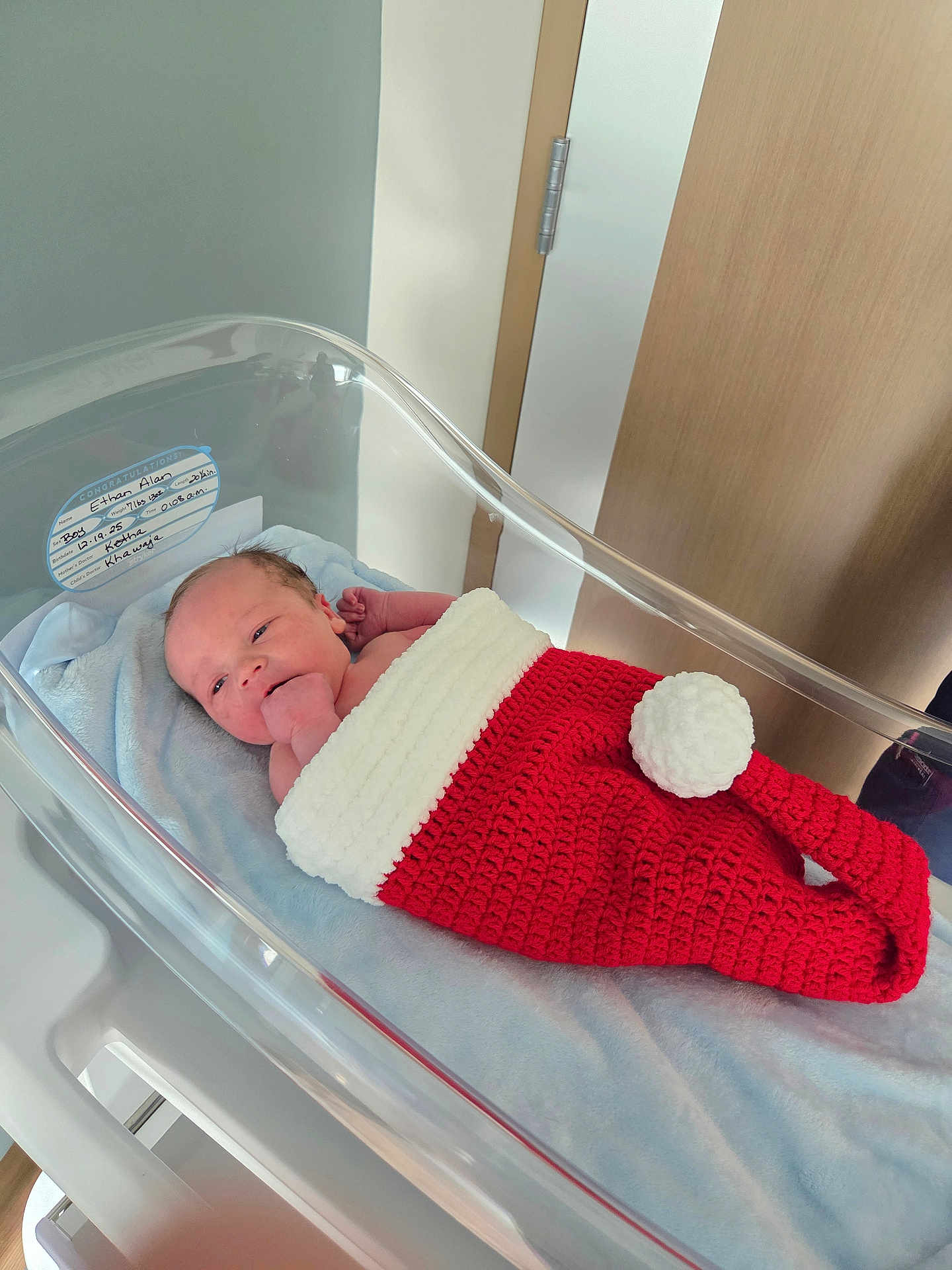 Ethan joined the competition — help win amazing prizes! newborn, baby, hospital, bassinet, crochet, red, white, blanket, infant, sleeping, hand, face, person, hospital_room, bed, cute, cozy, wrapped, lying_down, indoors