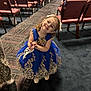 child, girl, dress, blue_dress, gold_embroidery, smiling, happy, posing, stage, auditorium, chairs, carpet, people, event, bow, white_shoes, patterned_clothing, floor, indoor, portrait
