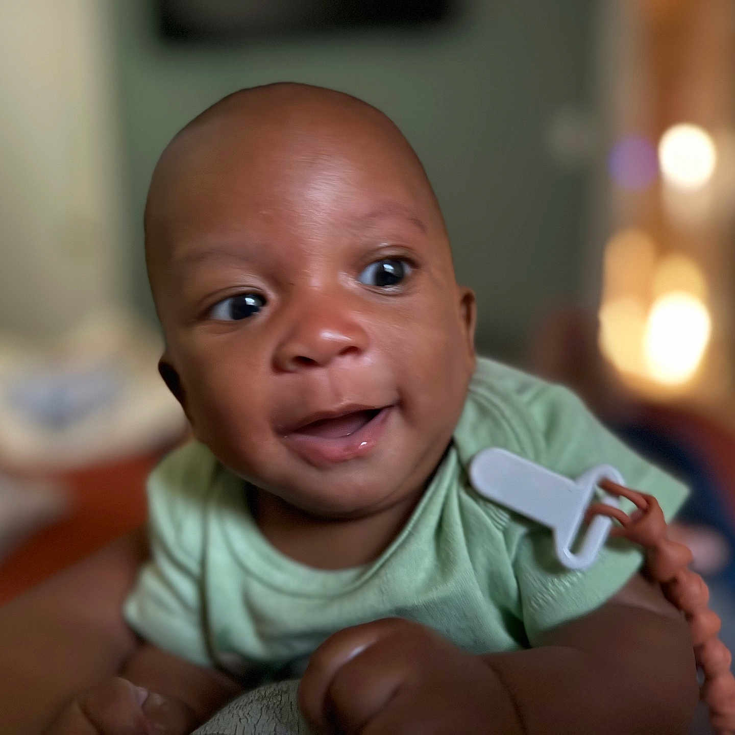 Mykah is registered to the contest to win money with this photo: baby, blurred_background, child, closeup, crawling, cute, expression, eyes, face, green_onesie, hand, happy, indoors, infant, pacifier_clip, person, portrait, skin, smiling, young
