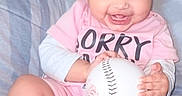 Suhana joined the competition — help win amazing prizes! baby, baseball, child, couch, cozy, curly_hair, cute, happy, holding_object, indoor, infant, person, pink_clothing, playful, portrait, seated, smiling, socks, soft_lighting, young_child