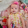 Olivia is registered to the contest to win money with this photo: baby, infant, child, pink_headband, floral_dress, plush_toys, blanket, soft_toys, book, colorful, cute, smiling, lying_down, indoors, playtime, happy, young_child, headband, fabric_book, comfortable