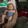 arm, baby, blanket, blue_onesie, closeup, comfortable, couch, curly_hair, hand, indoor, infant, nike_logo, person, phone, red_blanket, relaxing, resting, skin, tattoo, white_shirt