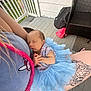 baby, backpack, blue_dress, bunny_design, closeup, hand, lap, newborn, outdoor, peaceful, person, porch, relaxing, shirt, skin, sleeping, tattoo, tulle_skirt, wicker_chair, wooden_floor