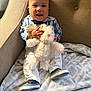 baby, child, smiling, plush_toy, stuffed_animal, chair, blanket, blue_shoes, bow_tie, white_pants, plaid_shirt, indoor, happy, cute, portrait, infant, couch, soft_toy, cozy, furniture