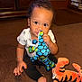 Julien joined the competition — help win amazing prizes! toddler, child, plush_toy, stuffed_animal, carpet, indoor, furniture, brown_carpet, white_shirt, black_pants, bracelet, barefoot, curly_hair, cute, playful, sitting, looking_at_camera, toy, orange_tiger, soft_toys