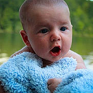 Noah is registered to the contest to win money with this photo: baby, blue_blanket, face, infant, outdoor, water, nature, trees, expression, skin, eyes, mouth, hand, portrait, candid, child, young, soft_texture, closeup, serene