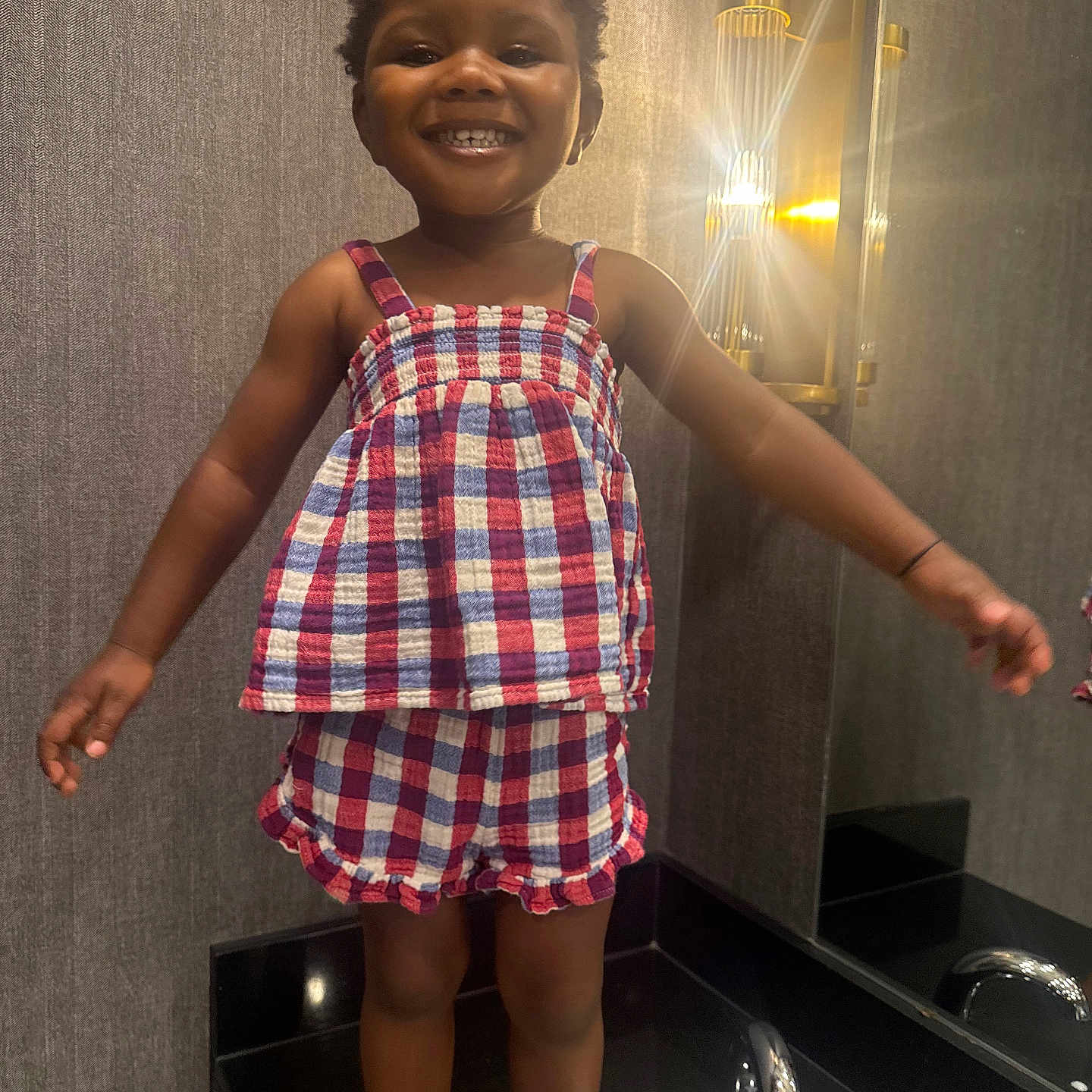 Amara joined the competition — help win amazing prizes! child, toddler, smile, bathroom, sink, mirror, lamp, light, checkered_outfit, clothing, happy, standing, interior, wall, reflection, face, person, cute, hair, barefoot