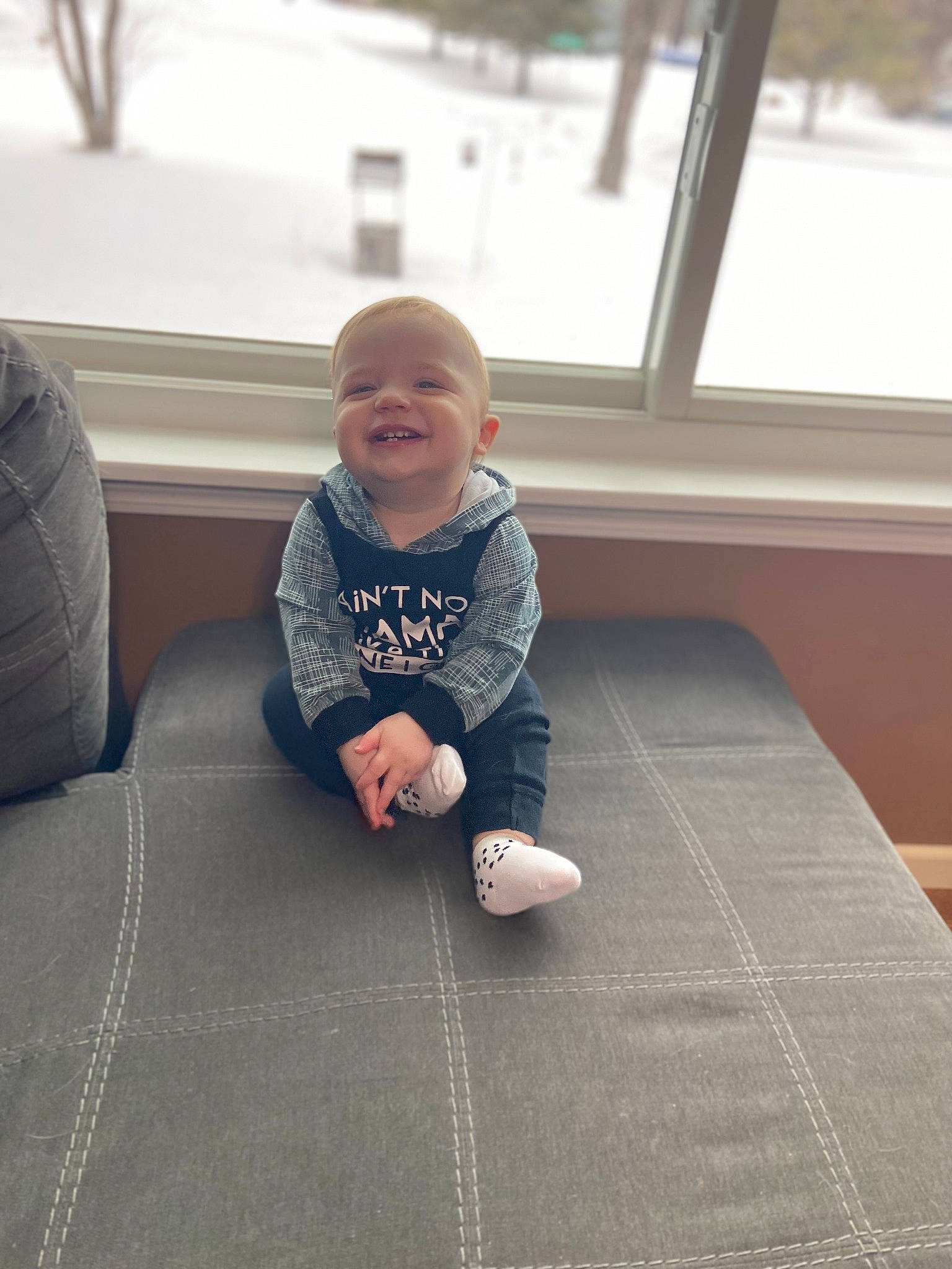 Jameson is registered to the contest to win money with this photo: child, comfort, facial_expression, floor, flooring, foot, fun, grey, happy, hardwood, head, human_leg, joy, knee, person, sitting, skin, sleeve, smile, t_shirt
