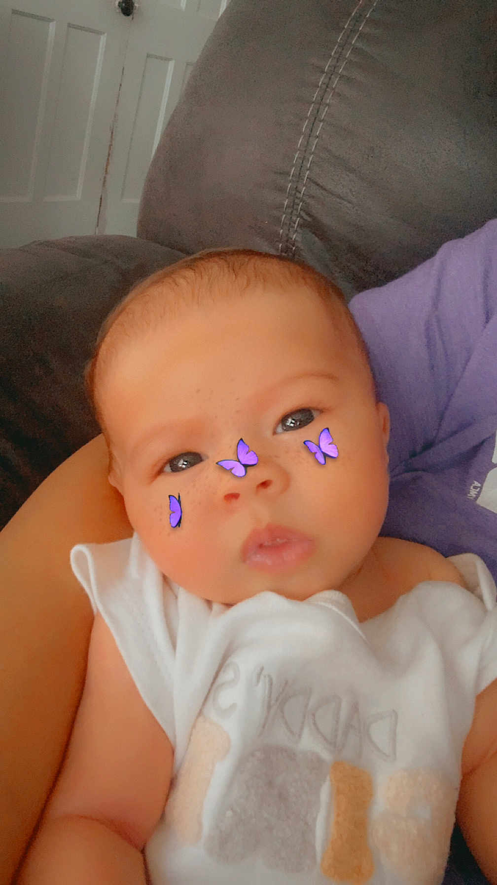 Ivy joined the competition — help win amazing prizes! baby, infant, face, purple_butterfly_stickers, freckles, white_clothing, person, arm, couch, indoor, door, head, sitting, soft_light, closeup, child, cute, holding, purple_shirt, skin