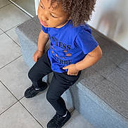 Deyvon participe au concours pour gagner de l'argent avec cette photo : child, curly_hair, blue_shirt, black_pants, bench, tile_floor, indoor, casual_clothing, seated, thoughtful, person, young, modern_interior, footwear, looking_away, hairstyle, contemplative, monochrome_floor, relaxed_pose, daylight