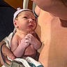 Ryker is registered to the contest to win money with this photo: newborn, baby, infant, child, portrait, cuddling, adult, parent, family, close_up, face, hands, hat, headband, blanket, striped_blanket, indoor, warm_lighting, tender, photography