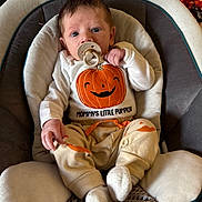 Ryker joined the competition — help win amazing prizes! baby, infant, child, portrait, sitting, bouncer, pacifier, pumpkin, halloween, costume, clothing, white_outfit, orange, smiling_pumpkin, indoor, cozy, chair, blanket, facial_expression, photography