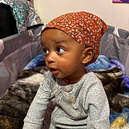 Xavier joined the competition — help win amazing prizes! baby, blanket, child, clothing, colorful, curious, face, gray_pajamas, headscarf, home, indoor, orange, person, playpen, portrait, quilt, seated, soft_texture, toddler, young_child